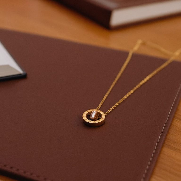 Collier en or avec un pendentif circulaire posé sur un carnet marron.