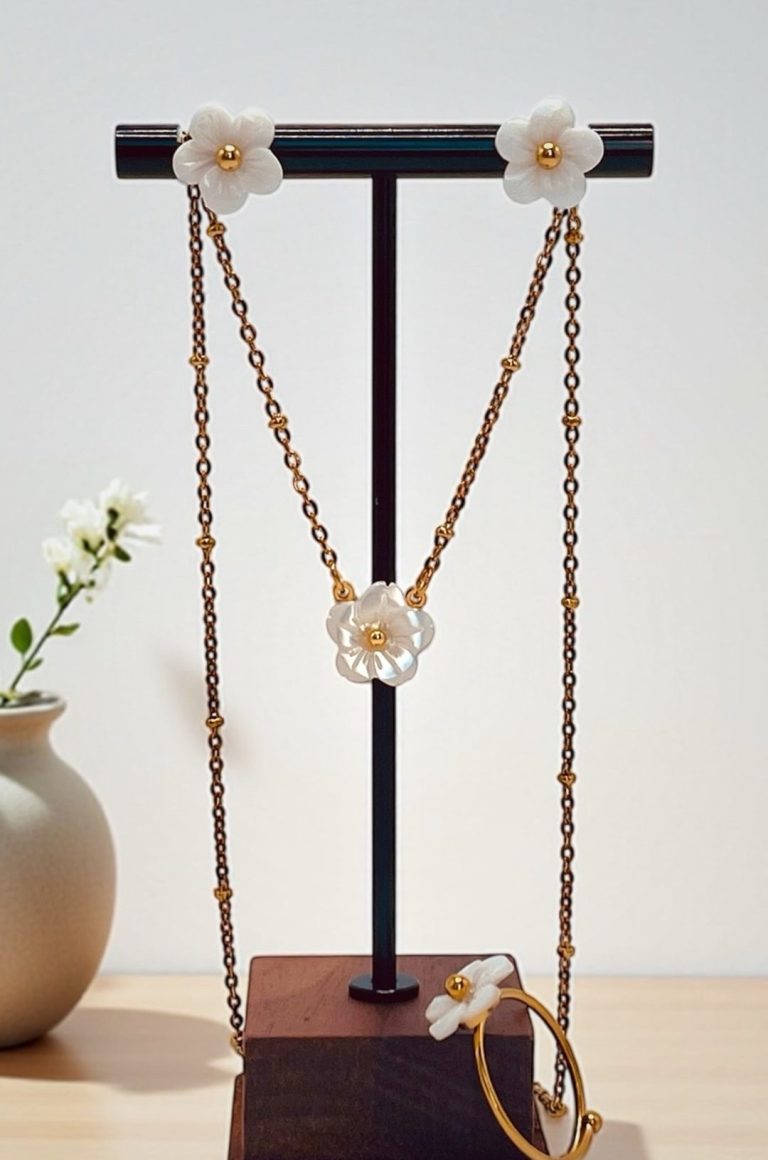 Collier et bracelet en bijou avec fleurs blanches sur support en bois.
