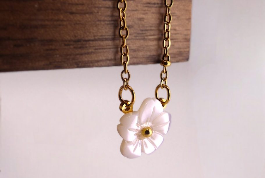 Collier en chaîne dorée avec une fleur blanche en pendentif.